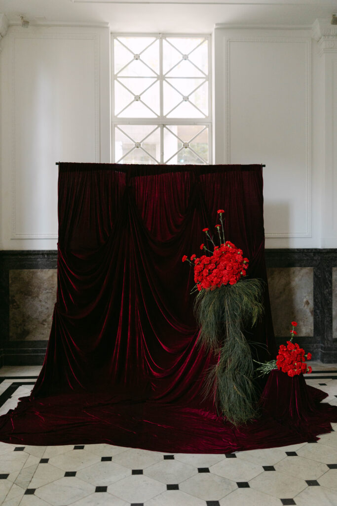 deep burgundy draped backdrop with bright red floral installations wedding trend