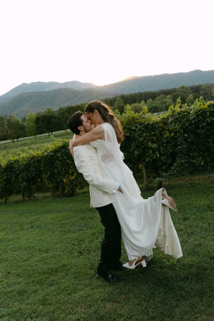 couple embracing in the field with mountains in the background at Feathertop Winery